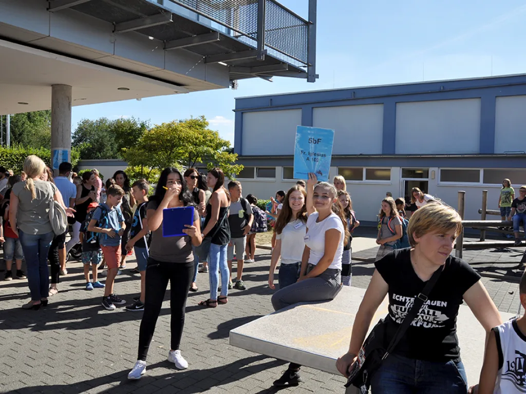 Besucher stehen auf dem Schulhof zusammen, im Hintergrund das Schulgebäude.